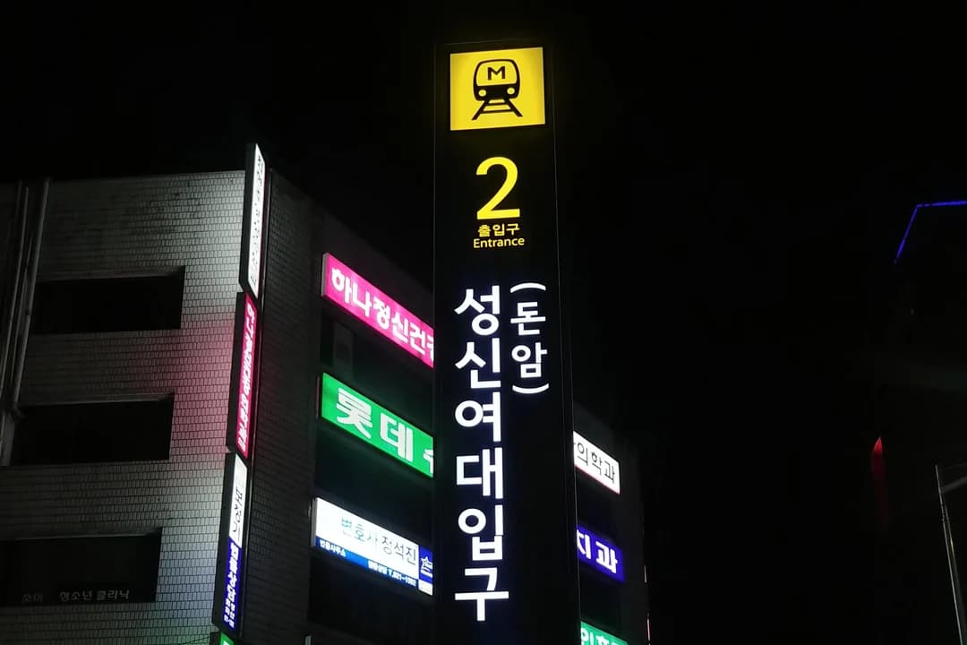 A tall lit exit sign at night showing the exit number 2 and the station name in Korean and English