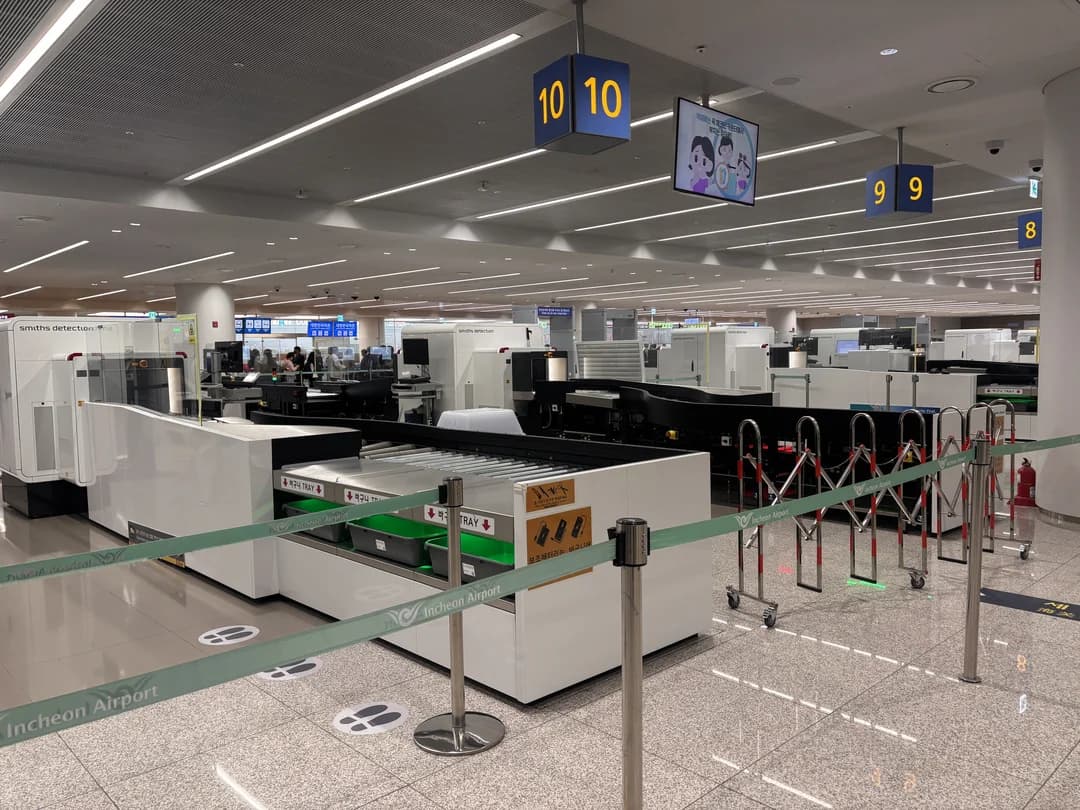 An airport inspection area with X-ray machines, trays and queue barriers
