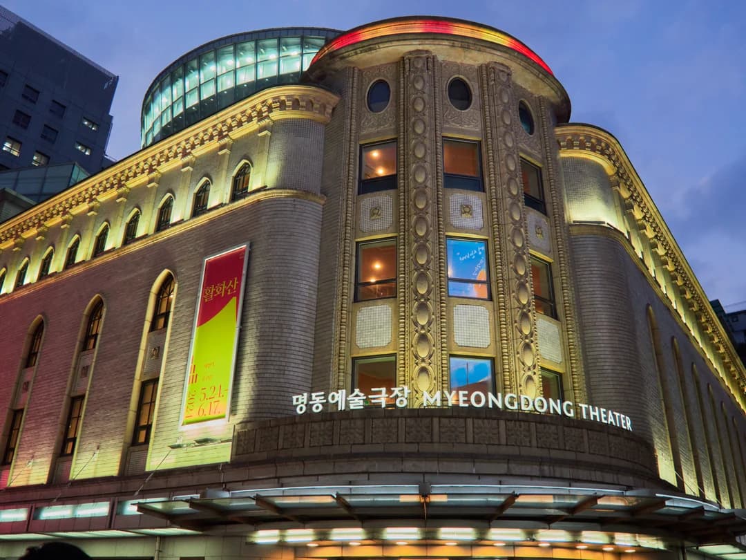 The curved, floodlit façade of Myeongdong Theater at dusk in Seoul’s main shopping district