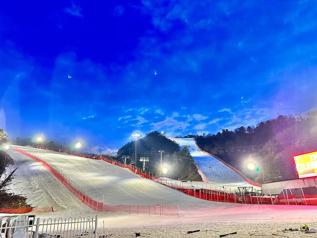 A floodlit ski slope at night with a large jump structure on the hillside (Elysian Gangchon)
